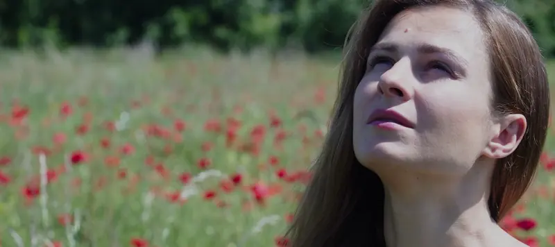 Une femme lève les yeux vers le ciel dans un champ de coquelicots.