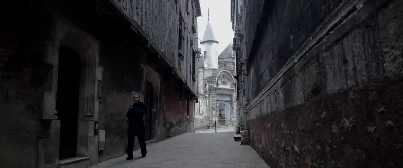 Une silhouette marche dans une ruelle ancienne menant à une tour.